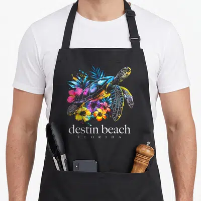 Scuba florida apron - Watercolor sea turtle with pink yellow blue flowers and destin beach florida text — shown on a black cotton canvas apron against a white background