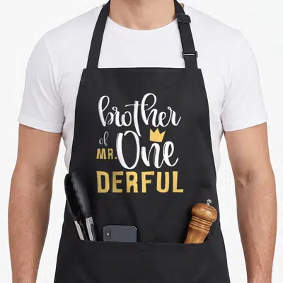 Onederful birthday apron - brother of mr one derful text with yellow crown on black bib apron — shown on a black cotton canvas apron against a white background