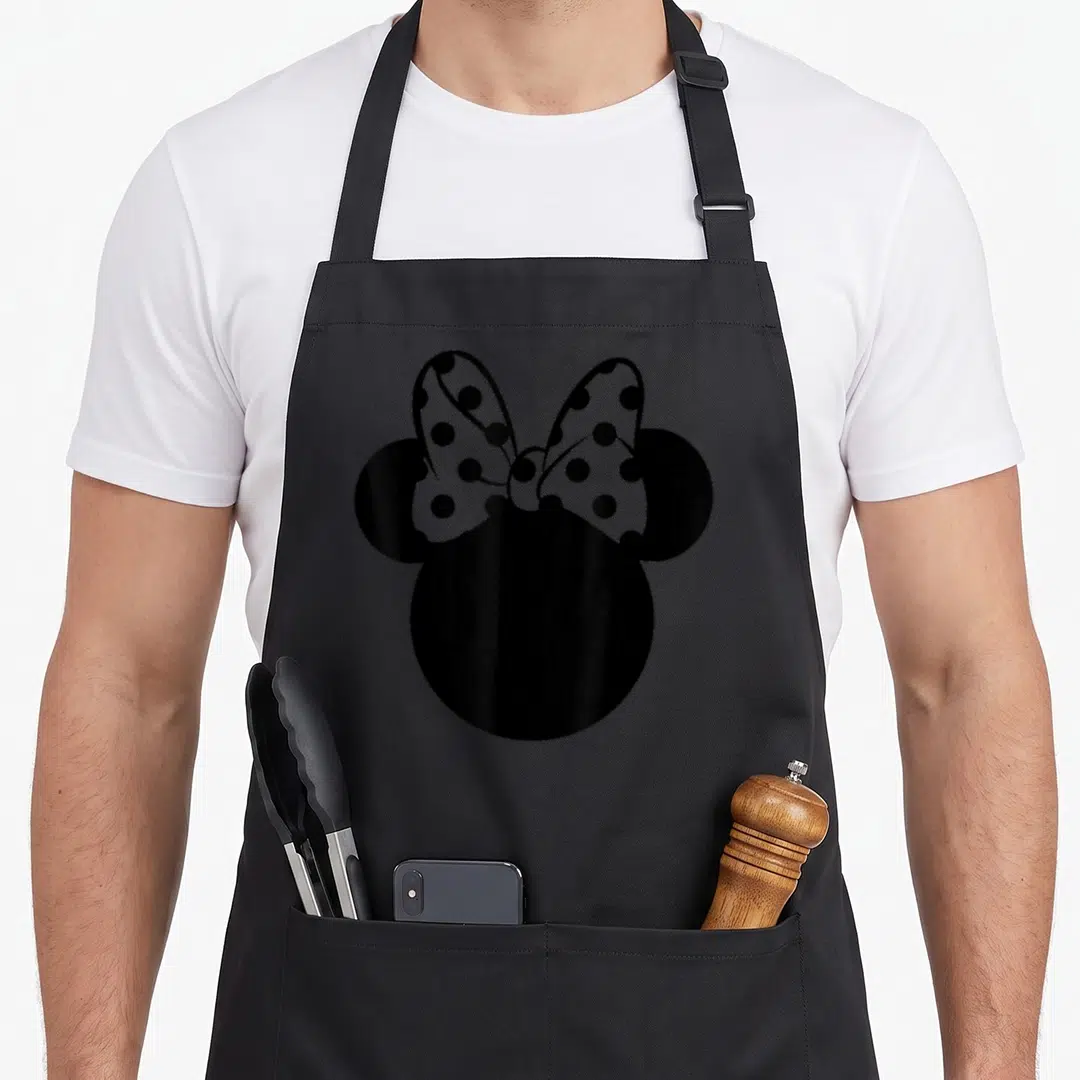 Polka bow apron - Black silhouette head with round ears and white bow with black polka dots — shown on a black cotton canvas apron against a white background