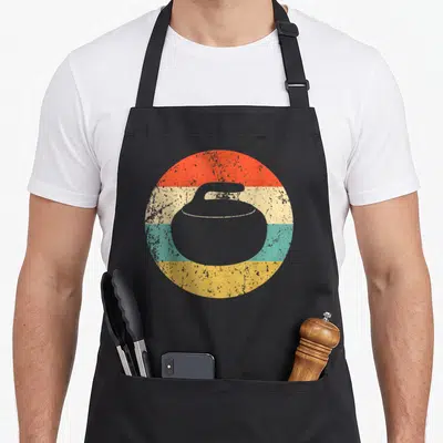 Funny curling stone apron - Grey curling stone silhouette over four horizontal stripes in red, cream, teal, and yellow — shown on a black cotton canvas apron against a white background