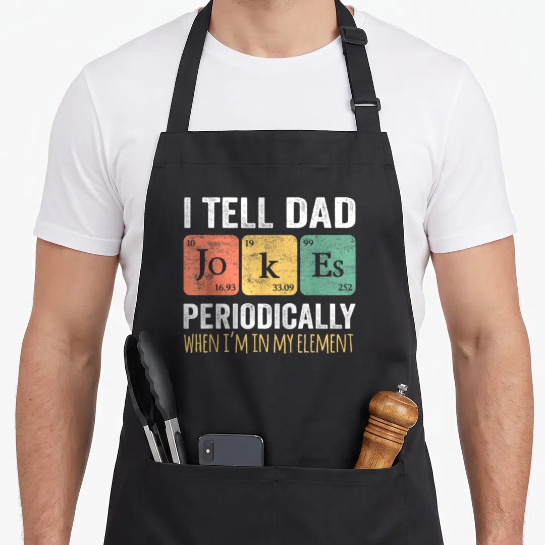 Periodically mens joke aprons - I Tell Dad Jokes Periodically when I'm In My Element periodic table graphic — shown on a black cotton canvas apron against a white background