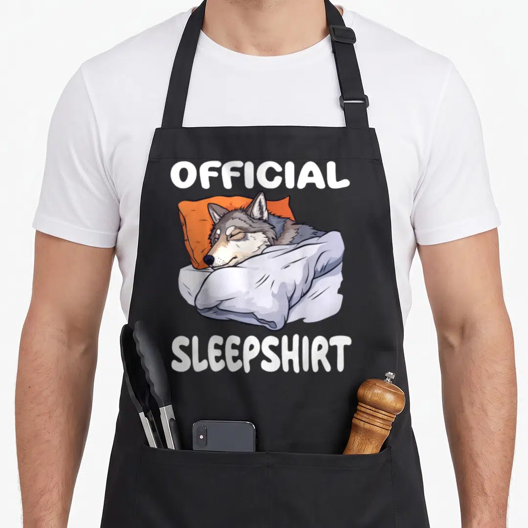 Wolf novelty apron - Sleeping grey wolf on orange pillow with official sleepshirt text — shown on a black cotton canvas apron against a white background