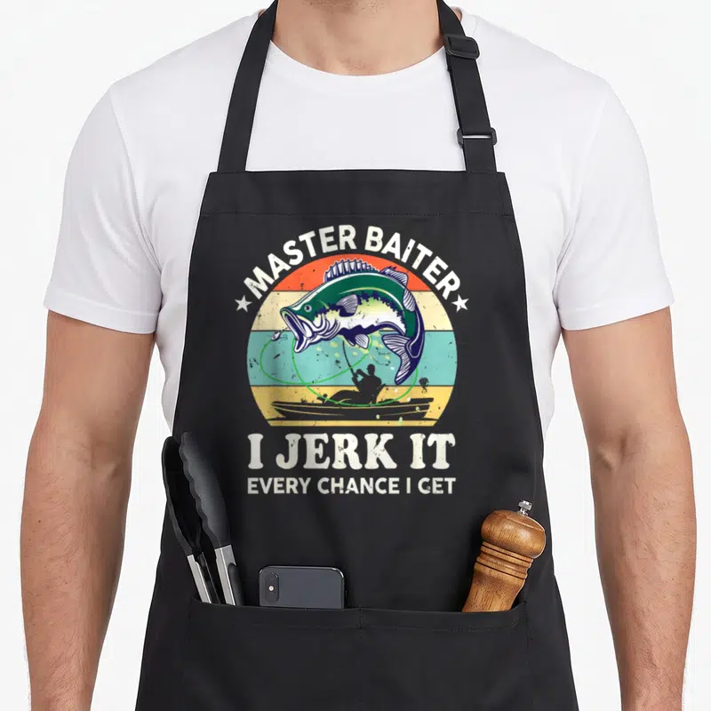 Kayak master apron - Retro circular sunset with jumping bass, fisherman silhouette, and text MASTER BAITER I JERK IT — shown on a black cotton canvas apron against a white background