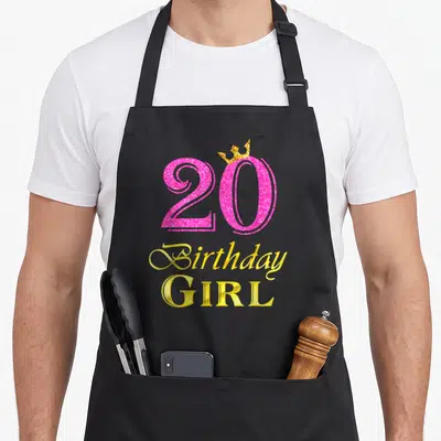 20th princess apron - Pink glitter number 20 with gold crown and stacked Birthday GIRL text — shown on a black cotton canvas apron against a white background