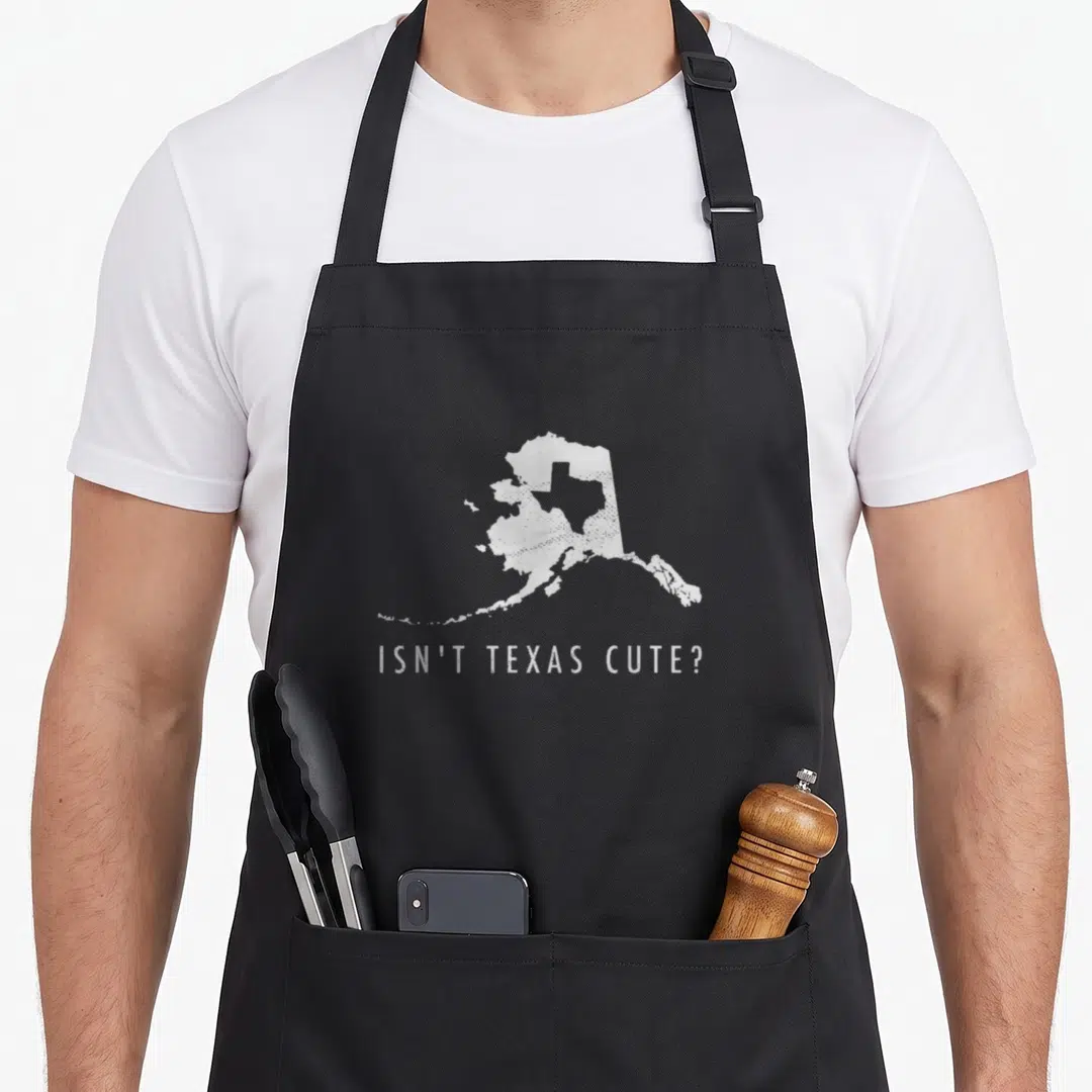 Alaska texas apron - White Alaska map with Texas silhouette and isn't texas cute text on black fabric — shown on a black cotton canvas apron against a white background