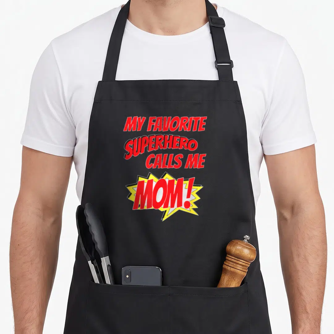 Call superhero apron - Red text reading My Favorite Superhero Calls Me Mom inside a yellow comic burst — shown on a black cotton canvas apron against a white background