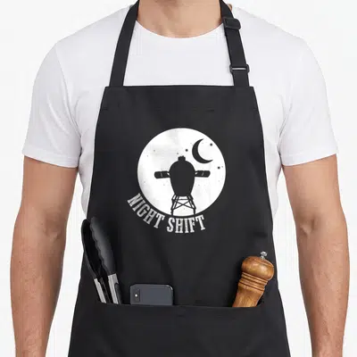 Night egg apron - Grey space capsule silhouette in white moon with arched NIGHT SHIFT text — shown on a black cotton canvas apron against a white background