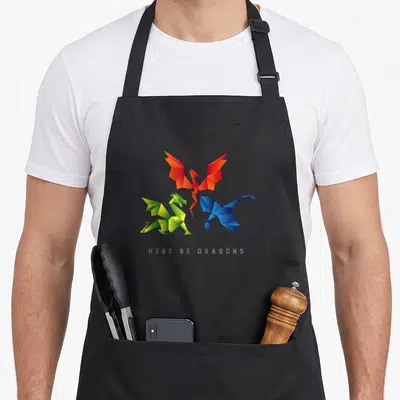 Scp dragon apron - Three geometric origami dragons in red green and blue above grey text HERE BE DRAGONS — shown on a black cotton canvas apron against a white background
