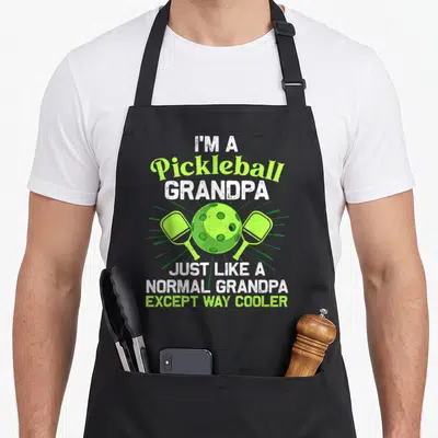 Pickleball grill daddy apron - Distressed text I'm a Pickleball Grandpa around lime ball and two paddles — shown on a black cotton canvas apron against a white background