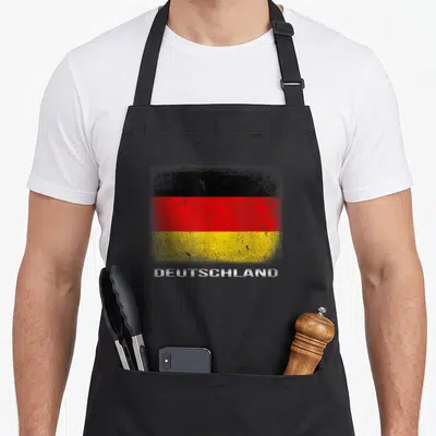 Souvenir german apron - Distressed German flag stripes above white DEUTSCHLAND text on apron front panel — shown on a black cotton canvas apron against a white background