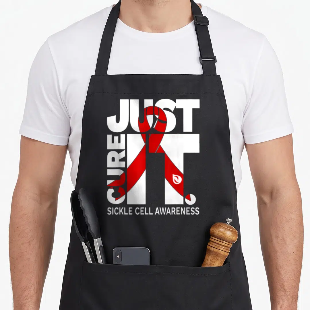 Cell ribbon apron - Just Cure It Sickle Cell Awareness text with red ribbon overlay — shown on a black cotton canvas apron against a white background