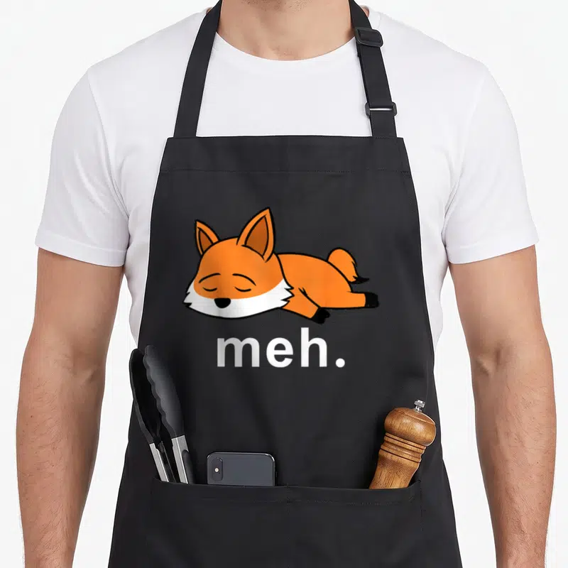 Fox meme apron - Cartoon orange fox lying down above white meh text on black fabric — shown on a black cotton canvas apron against a white background