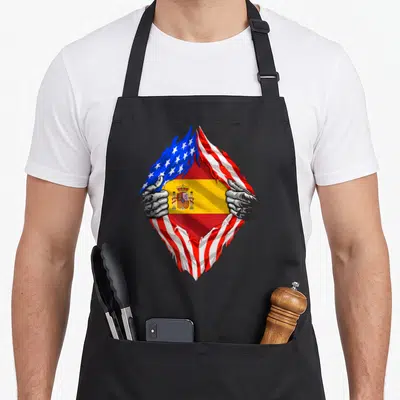 Spain american flag apron - Two grey hands tear USA flag to reveal Spanish red yellow blue flag design — shown on a black cotton canvas apron against a white background