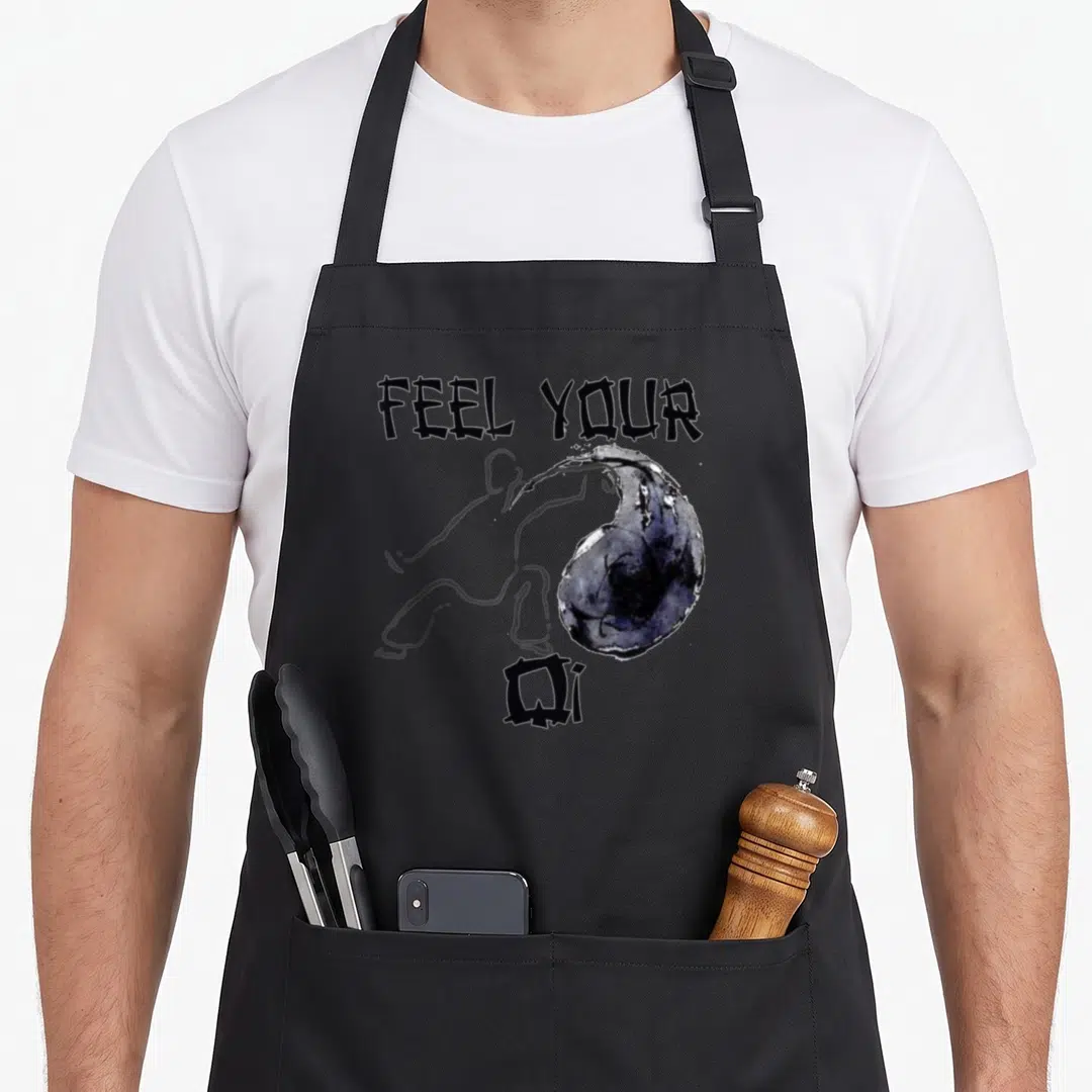 Feel qigong apron - Grey outline of person pushing dark blue sphere under text FEEL YOUR QI — shown on a black cotton canvas apron against a white background