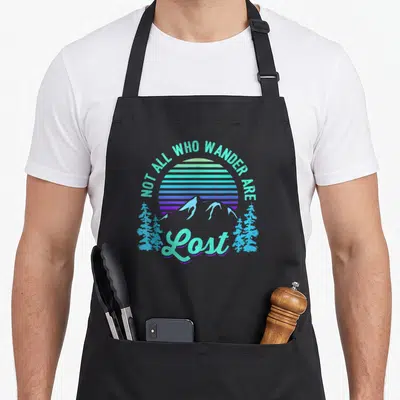 Wander mountain man apron - Retro mountain sun design with teal and purple text NOT ALL WHO WANDER ARE Lost — shown on a black cotton canvas apron against a white background