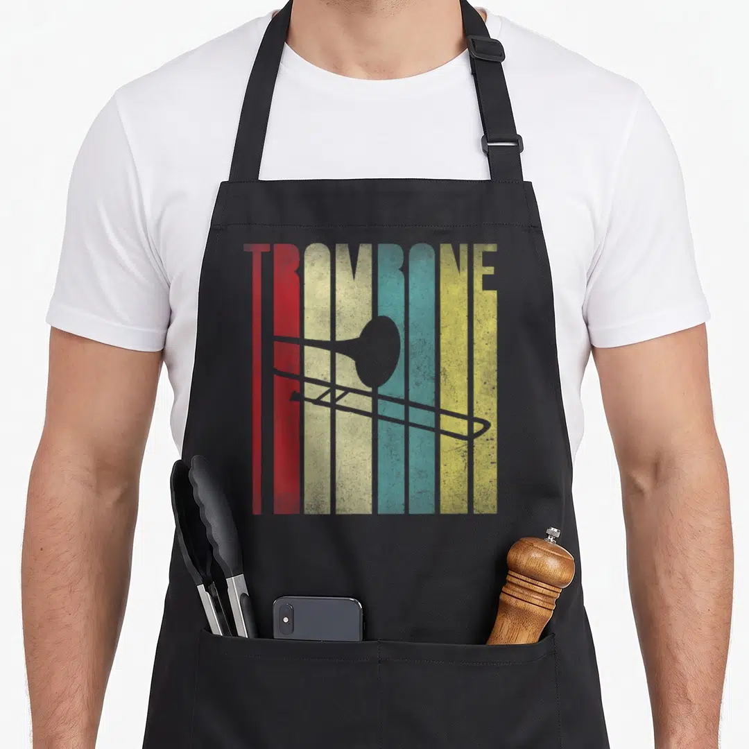 Player world music apron - TROMBONE text over grey silhouette on red orange cream blue yellow stripes — shown on a black cotton canvas apron against a white background