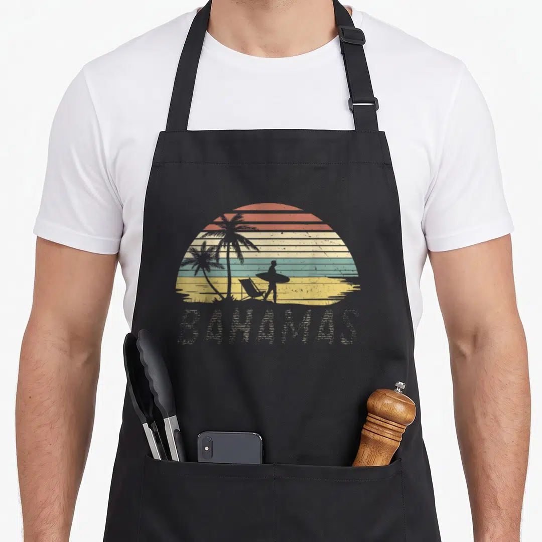 Bahamas flag nassau bahamian apron - Retro beach sunset with palm tree surfer and BAHAMAS text in red yellow teal grey — shown on a black cotton canvas apron against a white background