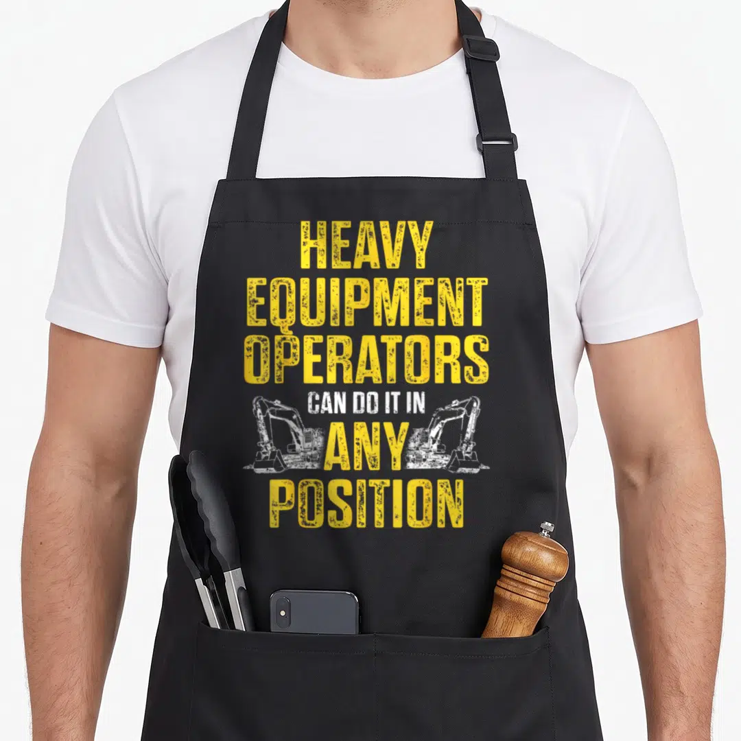 Position heavy canvas aprons - Yellow distressed text reading Heavy Equipment Operators Can Do It In Any Position — shown on a black cotton canvas apron against a white background