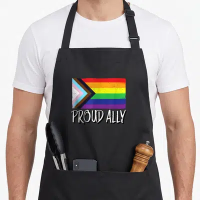 Proud gay pride apron - Distressed rainbow flag with black brown and white chevrons above PROUD ALLY text — shown on a black cotton canvas apron against a white background