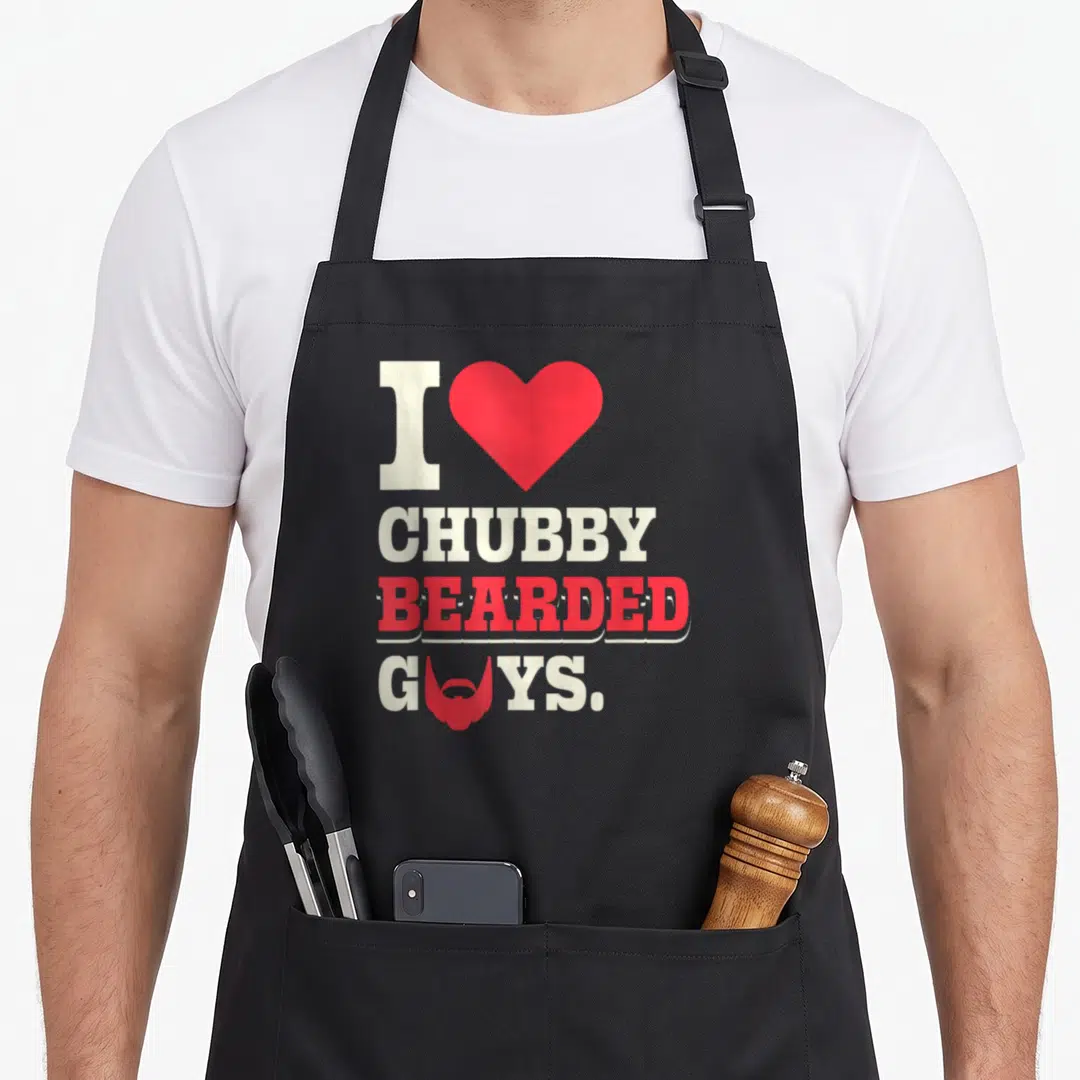 Husband beard apron - Stacked I heart Chubby Bearded Guys text with red beard icon replacing O — shown on a black cotton canvas apron against a white background