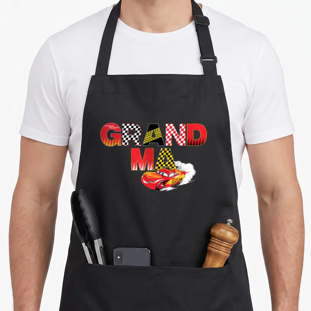 Trip car apron - GRAND MA text with Lightning McQueen and checkered patterns in red, yellow, black, and white — shown on a black cotton canvas apron against a white background