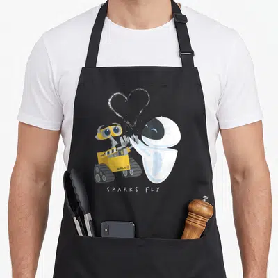 Spark e.a apron - Two cartoon robots holding hands with white heart and SPARKS FLY text — shown on a black cotton canvas apron against a white background