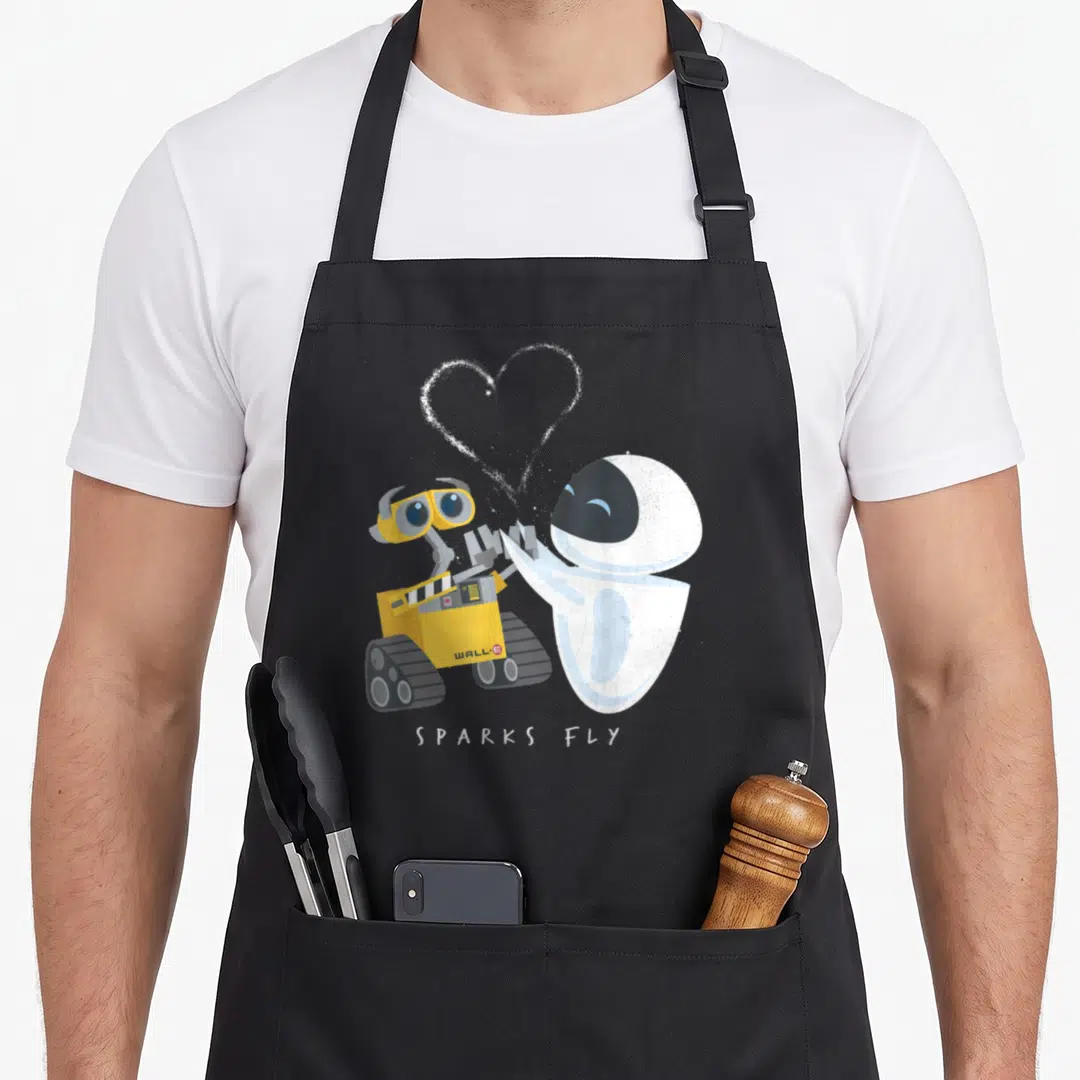 Spark e.a apron - Two cartoon robots holding hands with white heart and SPARKS FLY text — shown on a black cotton canvas apron against a white background