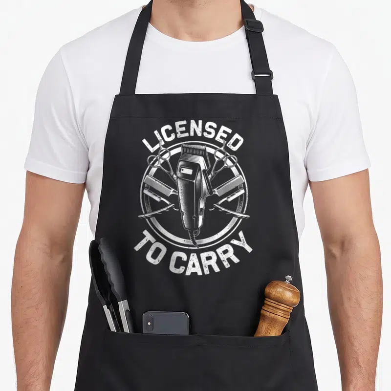 Stylist hairstyling apron - White distressed hair clipper and tools inside circle with arched text — shown on a black cotton canvas apron against a white background