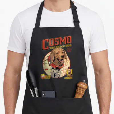 Guardian dog apron - Cosmo space dog in suit with want a zarg nut text and man portrait — shown on a black cotton canvas apron against a white background