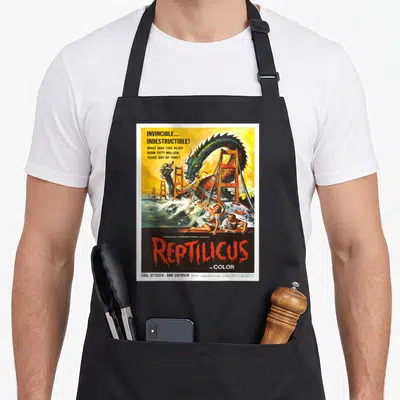 Reptilicus movie poster apron - Retro poster of green monster attacking red bridge with yellow sky and dripping red — shown on a black cotton canvas apron against a white background