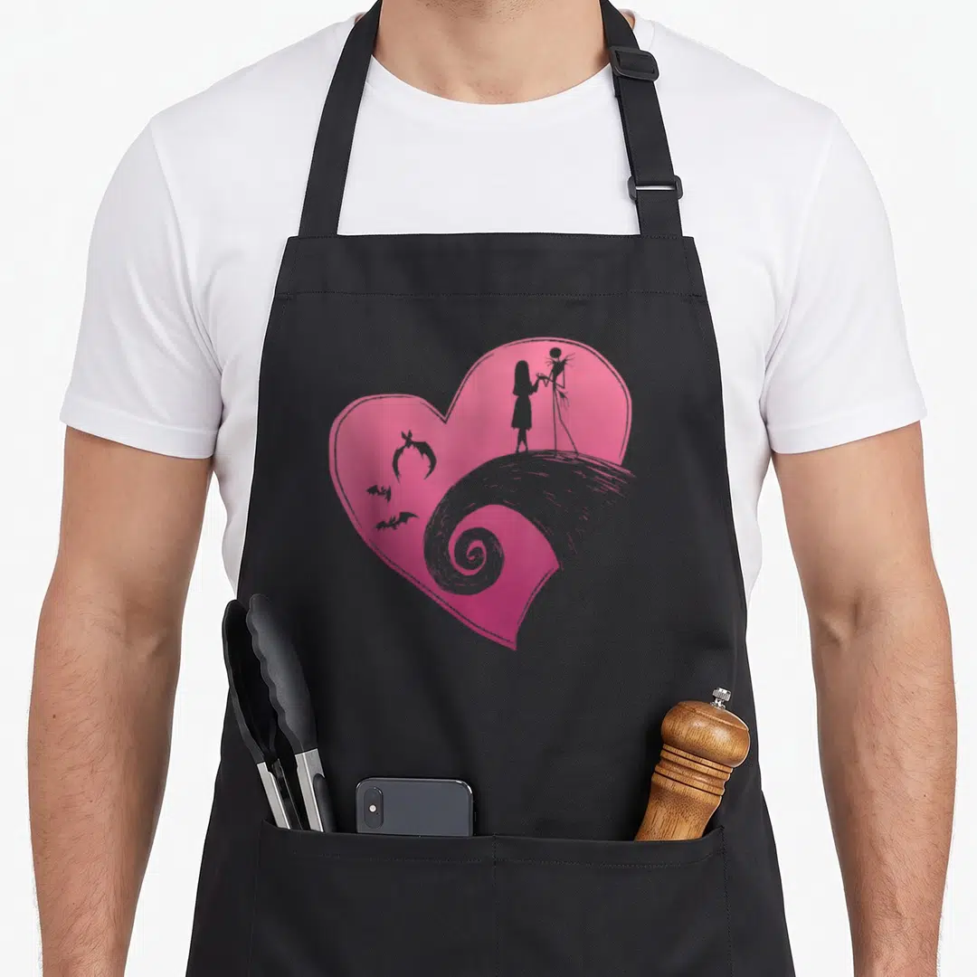 Jack sally christmas apron - Pink heart with grey character silhouettes, bats, and swirl design — shown on a black cotton canvas apron against a white background