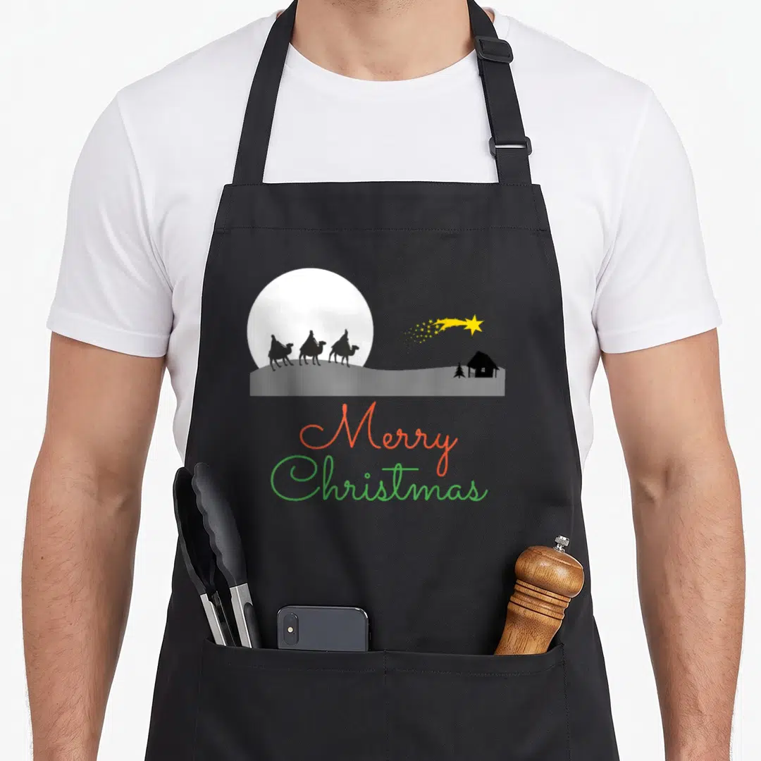 Three womens christmas apron - Silhouette of three wise men on camels under moon with Merry Christmas text in red — shown on a black cotton canvas apron against a white background