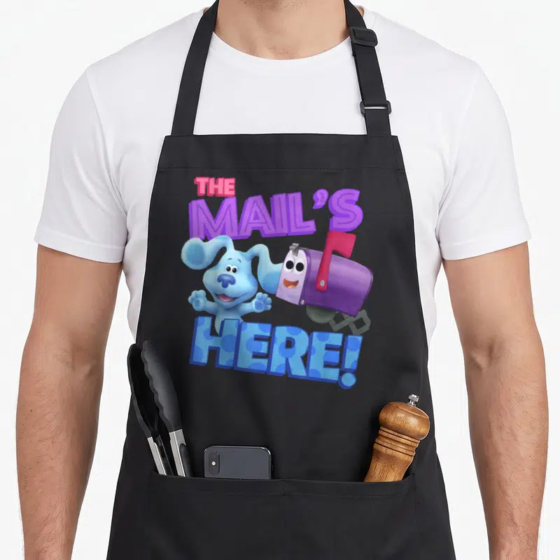 Mail clue apron - Blue dog and purple mailbox with THE MAIL'S HERE! text in cartoon style — shown on a black cotton canvas apron against a white background