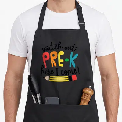 Pre watch out apron - Stacked watch out pre-k here i come text with horizontal yellow pencil drawing in cartoon style — shown on a black cotton canvas apron against a white background