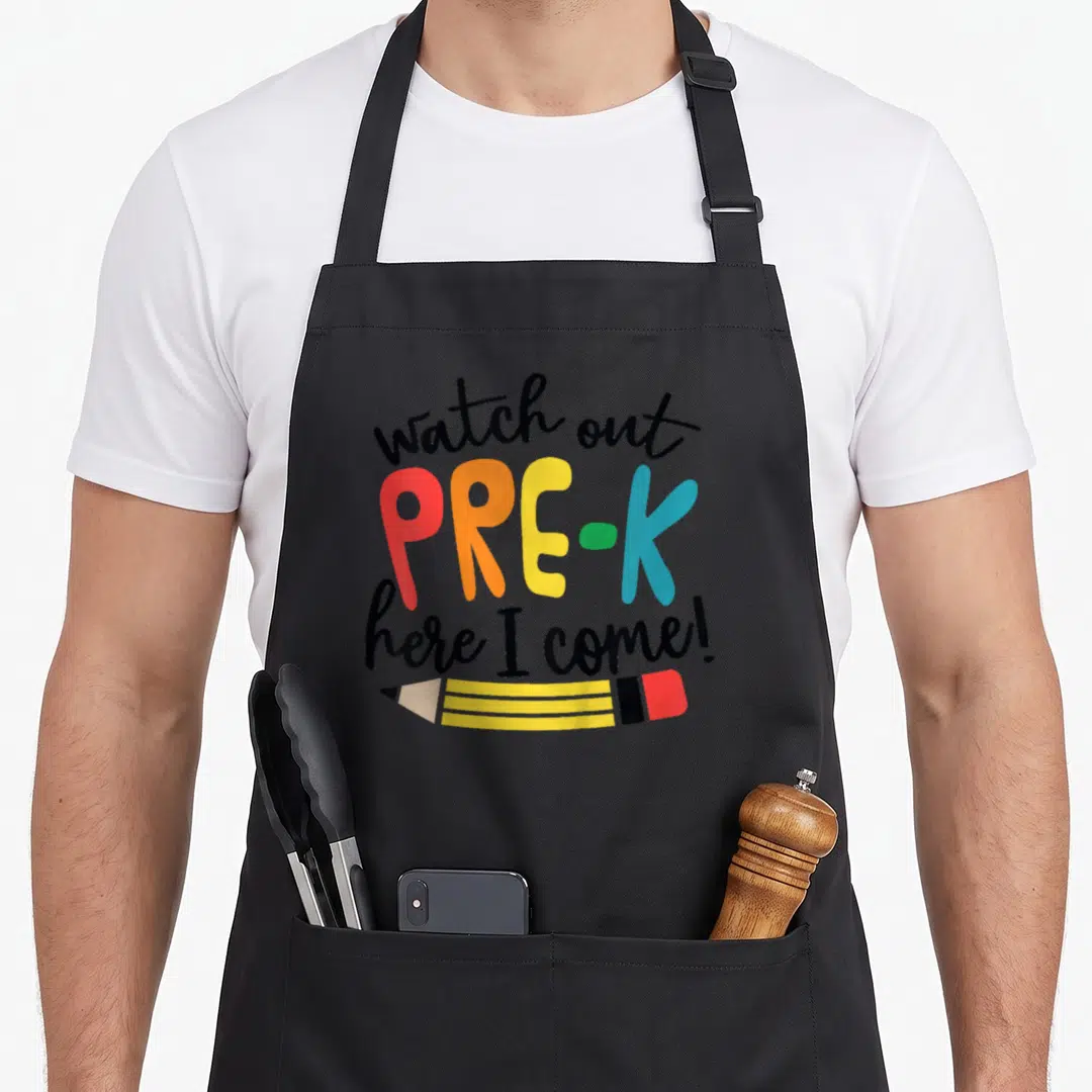 Pre watch out apron - Stacked watch out pre-k here i come text with horizontal yellow pencil drawing in cartoon style — shown on a black cotton canvas apron against a white background