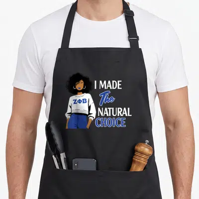 Zeta sorority apron - Woman in blue pants and white sweater with ZPhiB text next to I Made The Natural Choice slogan — shown on a black cotton canvas apron against a white background
