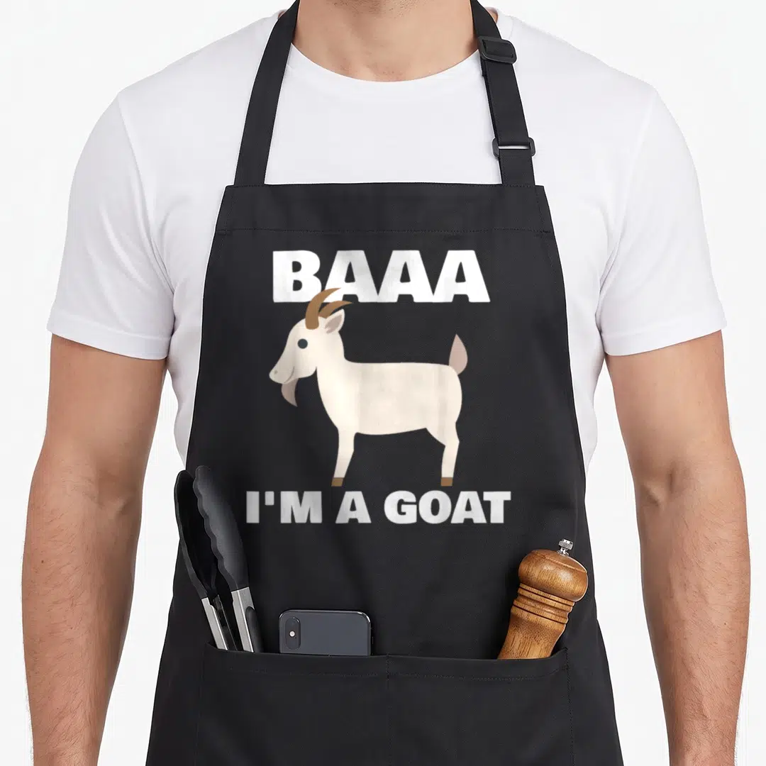 Baa cute halloween aprons - Cartoon goat between BAAA and I'M A GOAT text in white and brown — shown on a black cotton canvas apron against a white background
