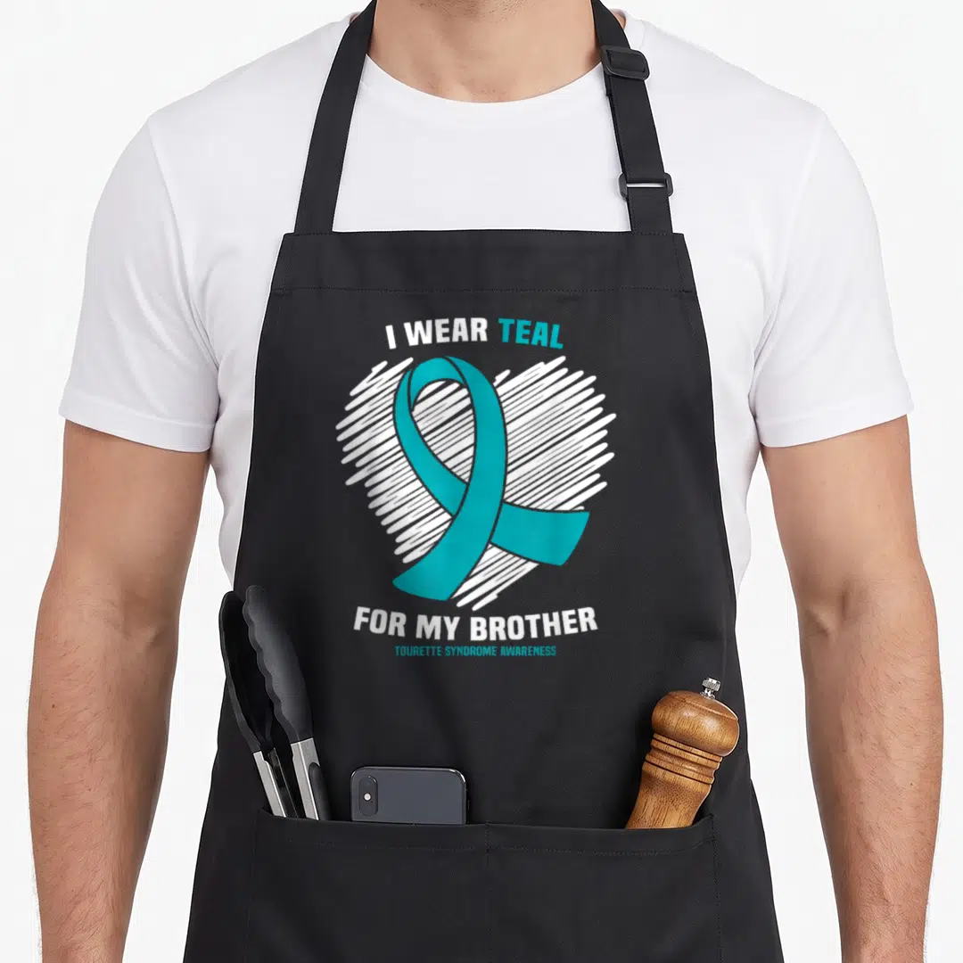 Brother tourette awareness apron - Teal awareness ribbon overlapping a white scribbled heart with text about wearing — shown on a black cotton canvas apron against a white background