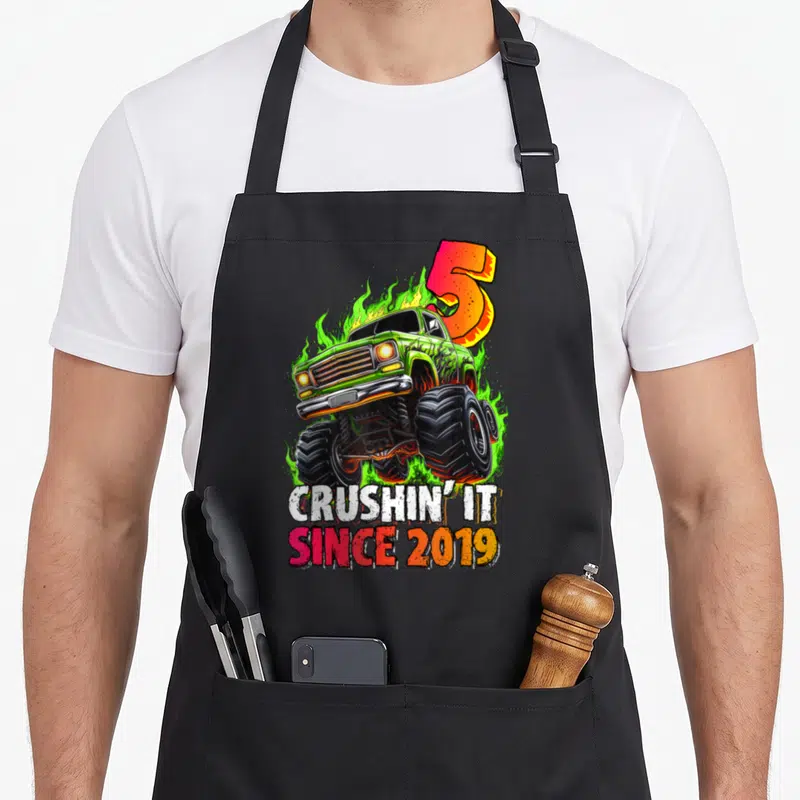 Monster 5th birthday truck apron - Green monster truck with flames and crushin it since 2019 text — shown on a black cotton canvas apron against a white background