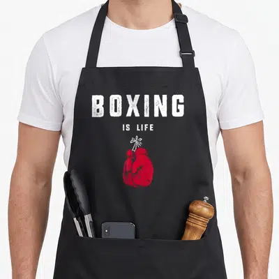 Cute boxing apron - Red boxing gloves tied with white string below stacked white distressed text reading BOXING IS LIFE — shown on a black cotton canvas apron against a white background