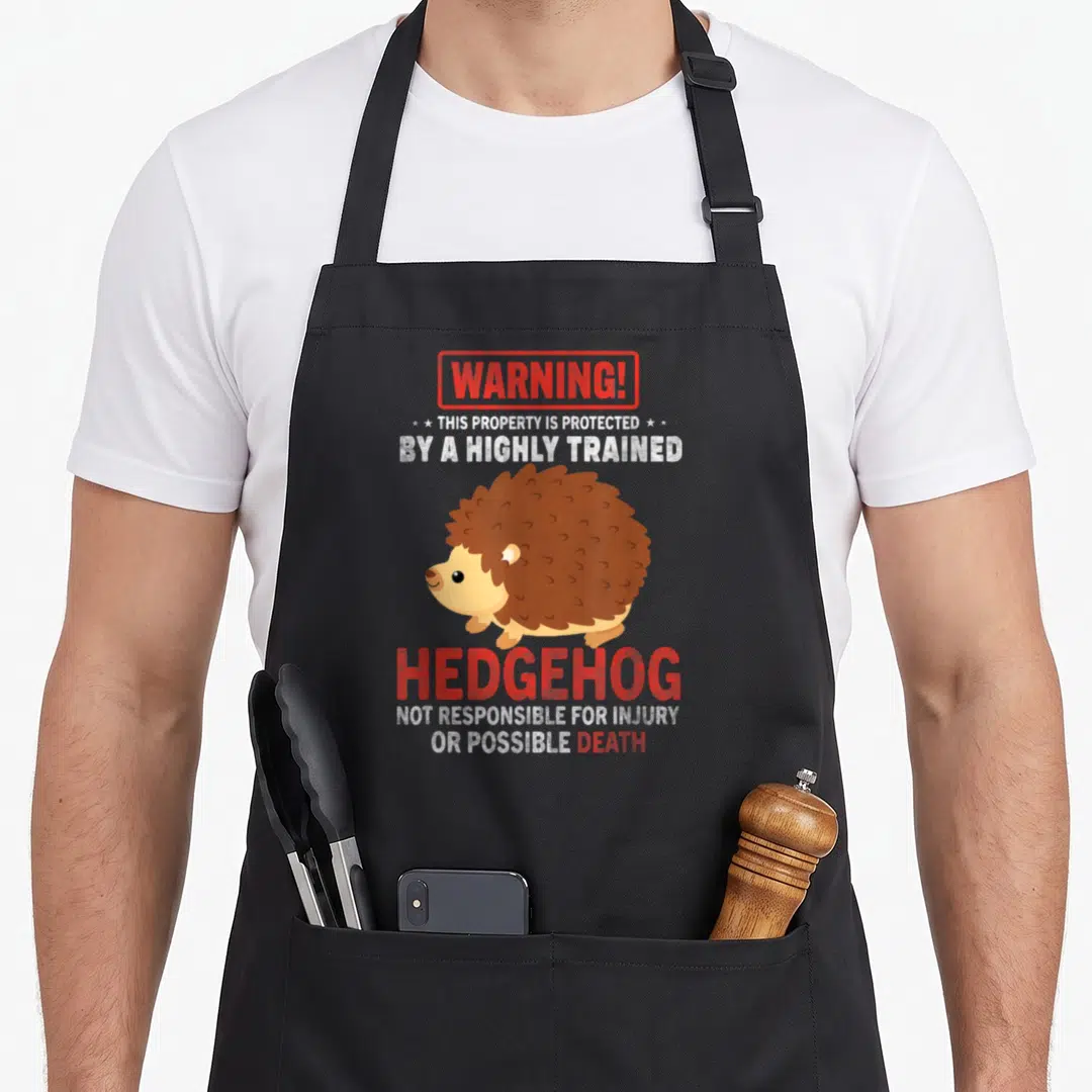 Vintage hedgehog animal apron - Cartoon brown hedgehog with red warning text about property protection and possible — shown on a black cotton canvas apron against a white background