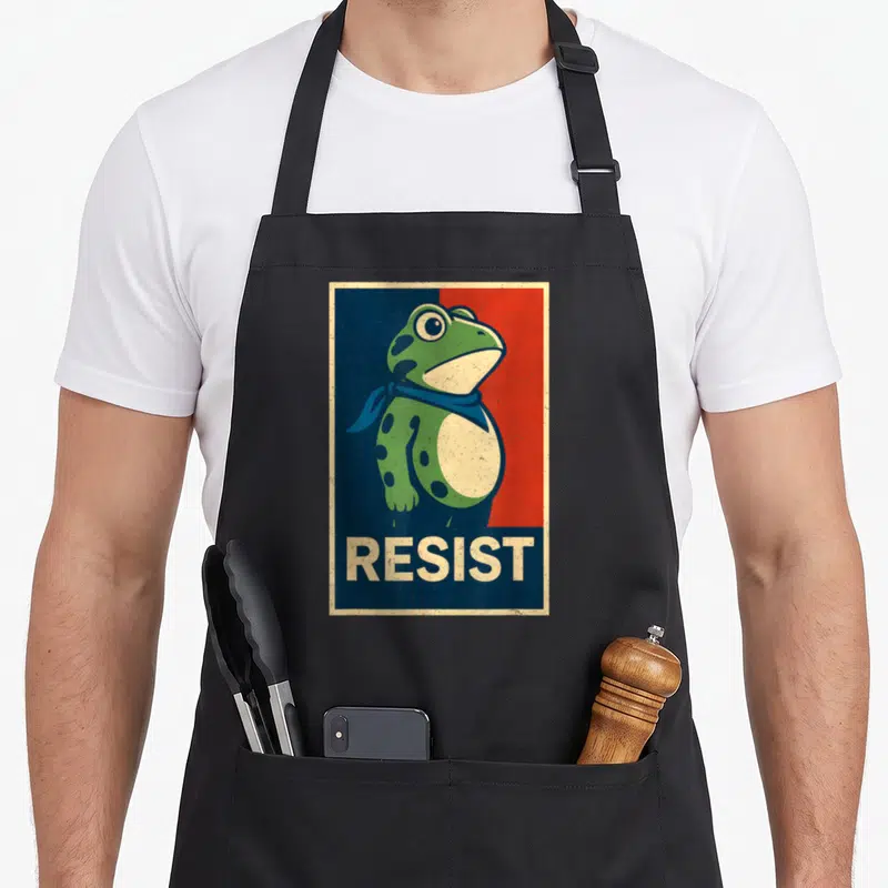 Portland frog aprons - Green frog in blue scarf against split blue red background with beige RESIST text bar — shown on a black cotton canvas apron against a white background