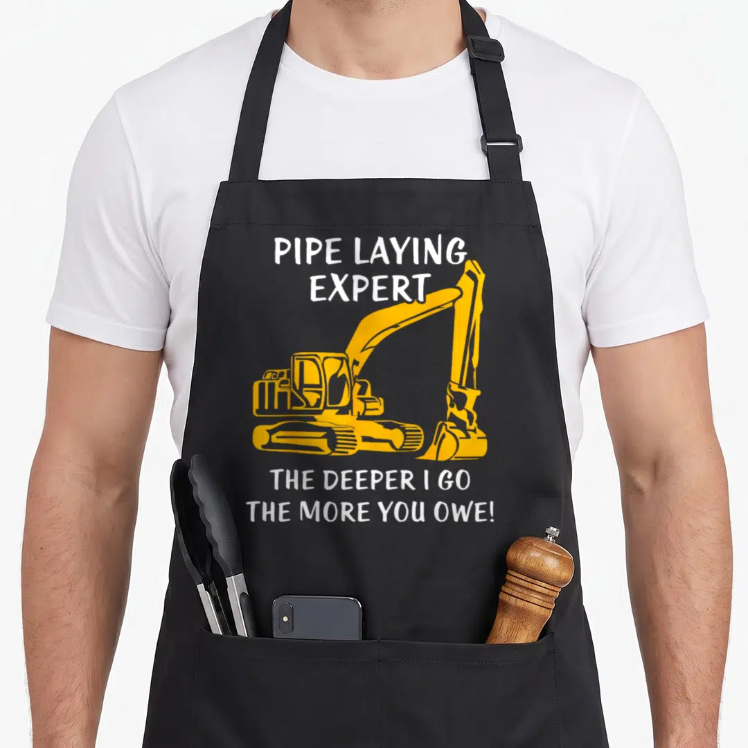 Pipe heavy canvas aprons - Yellow excavator graphic with white text pipe laying expert and deeper I go more you owe — shown on a black cotton canvas apron against a white background