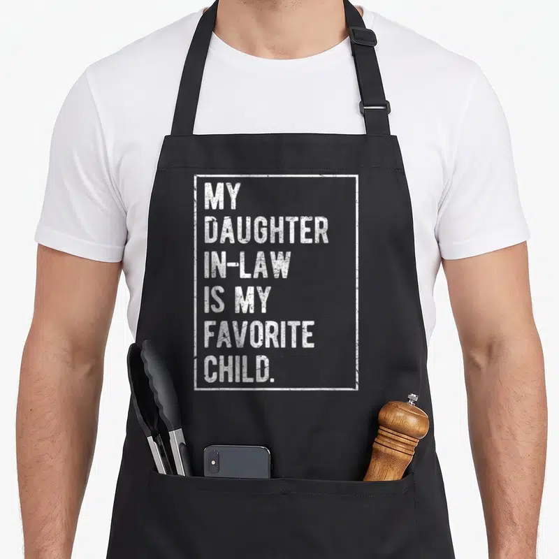 Cool daughter father day apron - White stacked text MY DAUGHTER IN-LAW IS MY FAVORITE CHILD inside distressed white — shown on a black cotton canvas apron against a white background