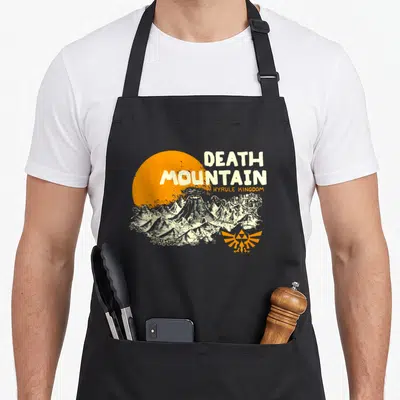 Hyrule mountain apron - Distressed Death Mountain print with orange sun and Hyrule Kingdom text — shown on a black cotton canvas apron against a white background