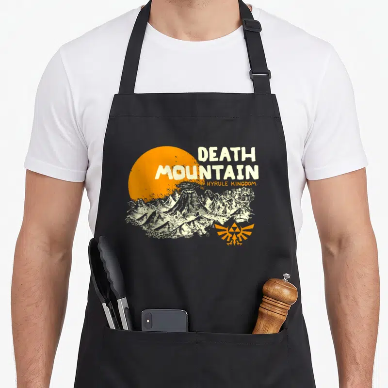 Hyrule mountain apron - Distressed Death Mountain print with orange sun and Hyrule Kingdom text — shown on a black cotton canvas apron against a white background