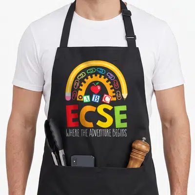 Early special aprons - Yellow pencil arch over red apple, ABC blocks, paperclips, and ECSE text — shown on a black cotton canvas apron against a white background