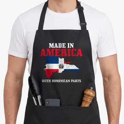 Funny dominican pride apron - Distressed red white and blue map of Dominican Republic with text Made in America — shown on a black cotton canvas apron against a white background
