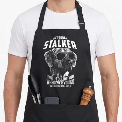 Rhodesian personal apron - White distressed dog head with sunglasses and text reading PERSONAL STALKER I WILL FOLLOW YOU — shown on a black cotton canvas apron against a white background