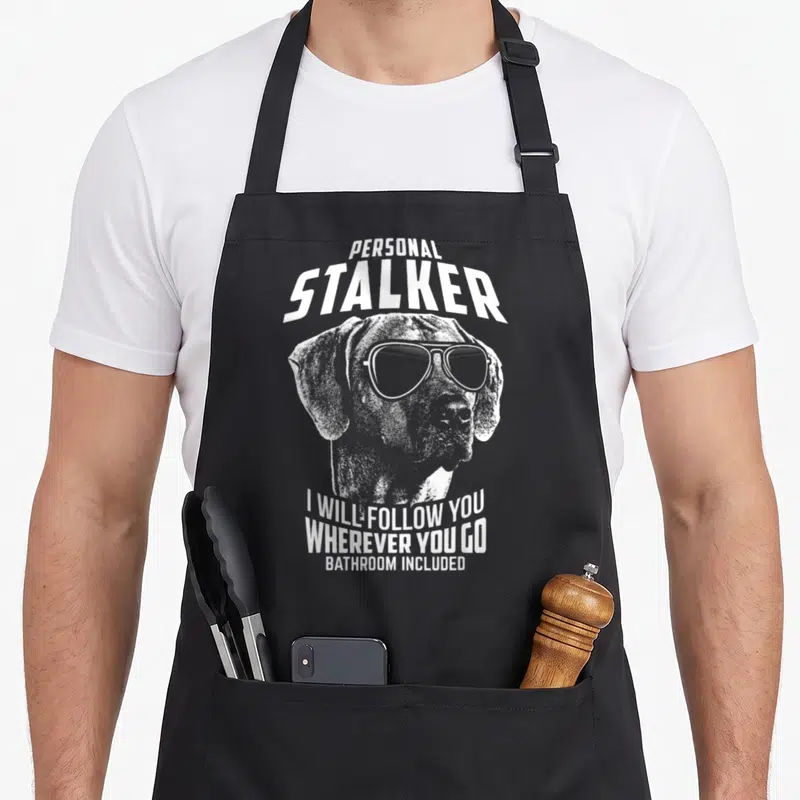 Rhodesian personal apron - White distressed dog head with sunglasses and text reading PERSONAL STALKER I WILL FOLLOW YOU — shown on a black cotton canvas apron against a white background